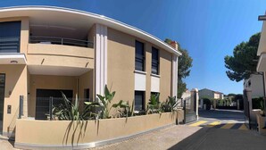 A modern two-story building with a curved facade, large windows, and a gated entrance. - Eco-responsible haven of peace in Golfe-Juan: new serviced apartment (Vallauris)