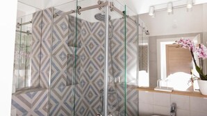 A modern bathroom with a glass-enclosed shower, patterned tiles, a sink, and a mirror with a potted orchid.