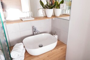 Een moderne badkamer met een wit wastafel, een houten aanrechtblad en potplanten.