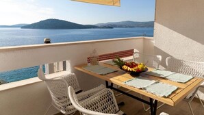 A balcony with a table, chairs, and a view of the sea and hills.