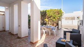 Un espace extérieur aménagé en terrasse, avec une table dressée pour les repas, entouré de chaises blanches et de meubles en osier.