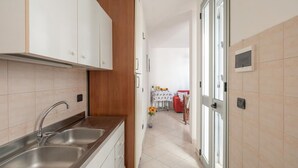 Une cuisine étroite avec un évier à deux bacs, des placards en bois et une vue sur un coin repas comprenant une table et des chaises.