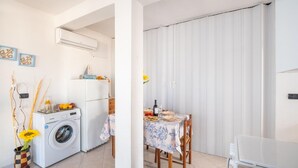 Une cuisine compacte équipée d’un lave-linge, d’un réfrigérateur et d’un coin repas avec une table dressée pour deux personnes.
