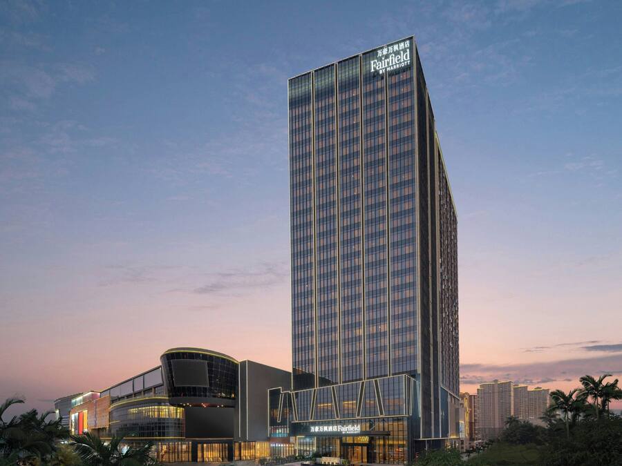 Un hotel moderno de altura con un llamativo letrero de "Fairfield by Marriott", que presenta una fachada de vidrio elegante y un diseño angular distintivo.
