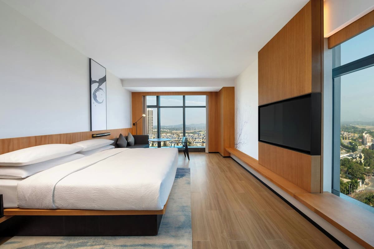 A modern hotel room with a large bed, a flat-screen TV, and a city view.
