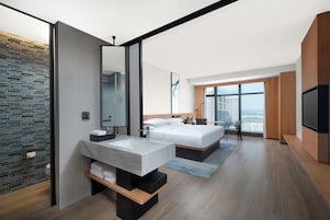 Una habitación de hotel moderna con una cama grande, un baño con lavamanos de mármol y vistas a la ciudad.