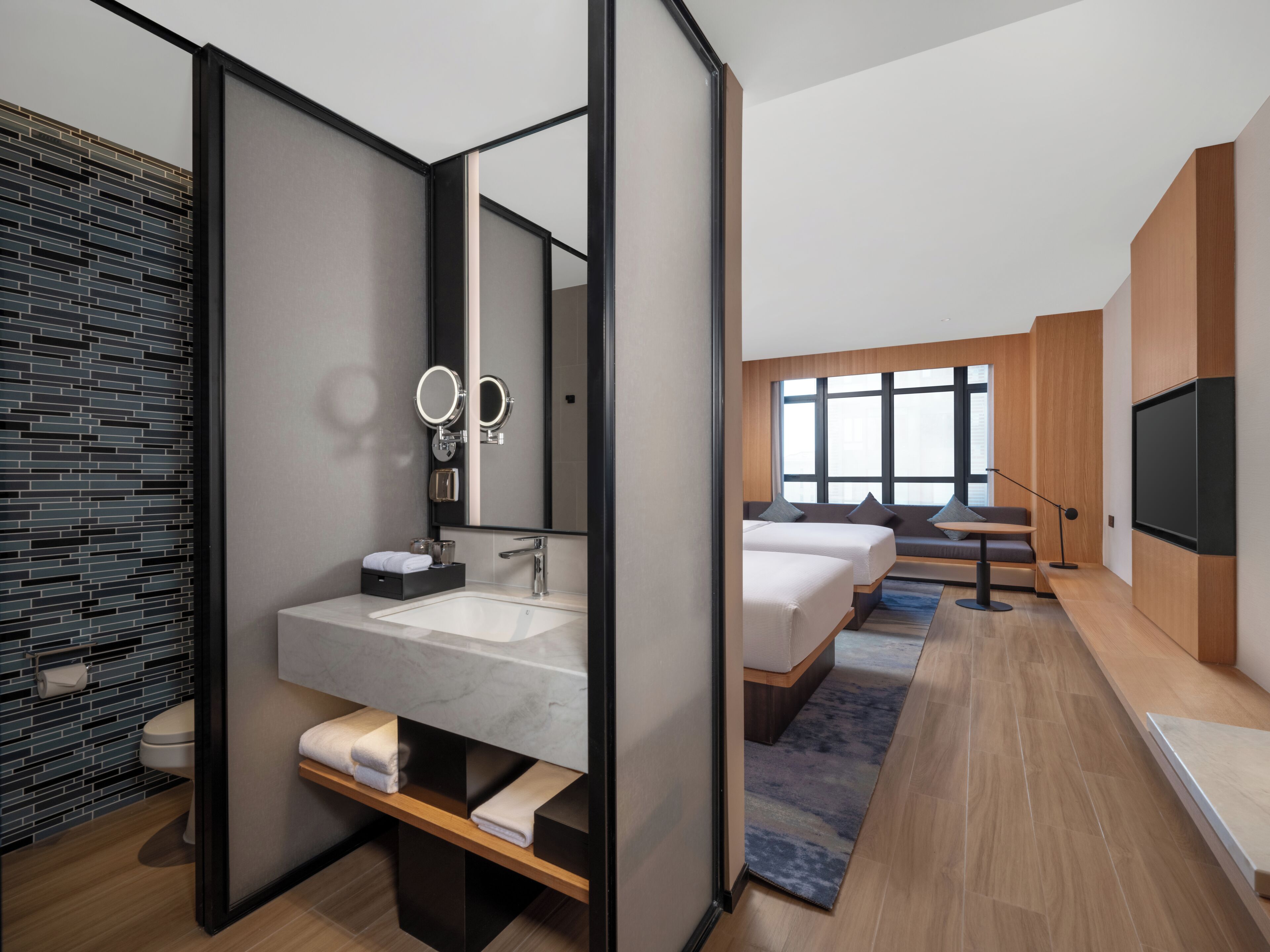 Una camera d'albergo moderna con un grande specchio, un lavabo in marmo, un pavimento in legno, una TV e un'area salotto con vista.