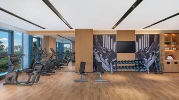 A modern gym with exercise equipment, large windows, and a wall-mounted TV.