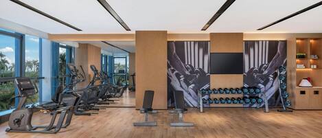 Un gimnasio moderno con equipo de ejercicio, ventanas amplias y un televisor instalado en la pared.
