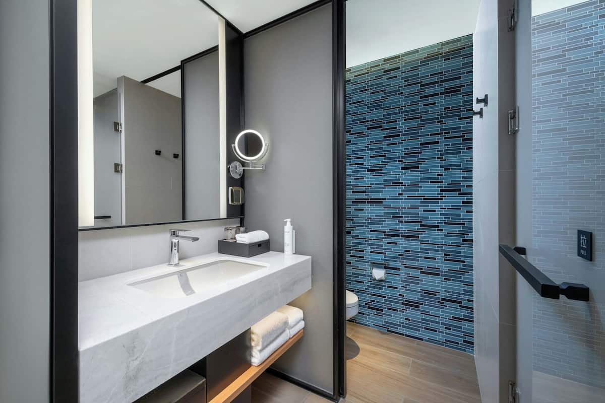 A modern bathroom with a large mirror, white sink, and a blue-tiled shower area.