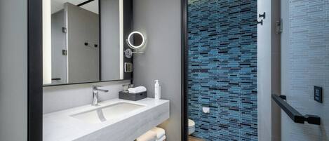A modern bathroom with a large mirror, white sink, and a blue-tiled shower area.