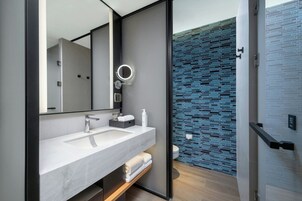 Un baño moderno con un espejo grande, un lavabo blanco y una zona de ducha con azulejos azules.