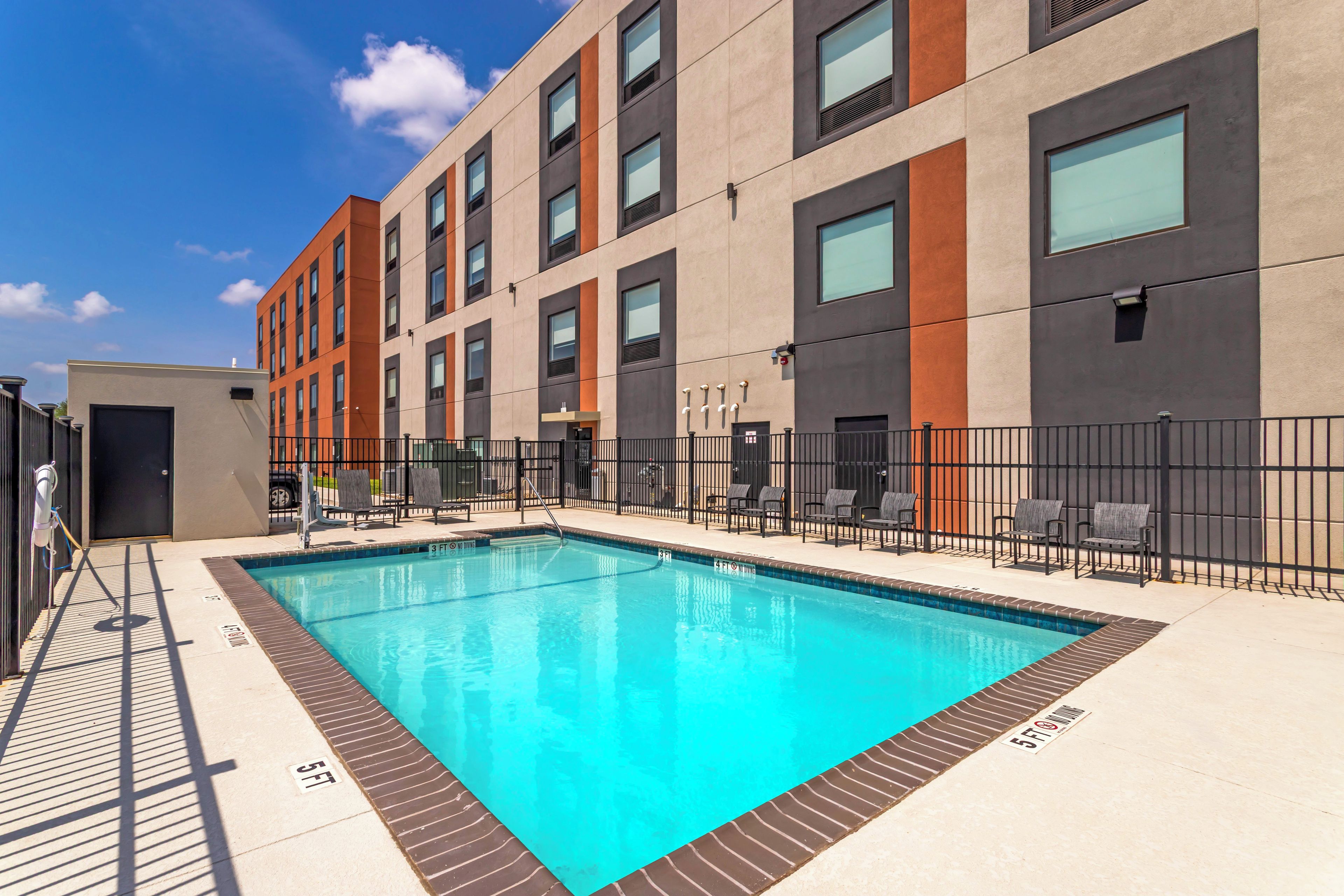 A modern building with a swimming pool, outdoor seating, and a clear sky.