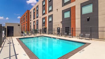 A modern building with a swimming pool, outdoor seating, and a clear sky.