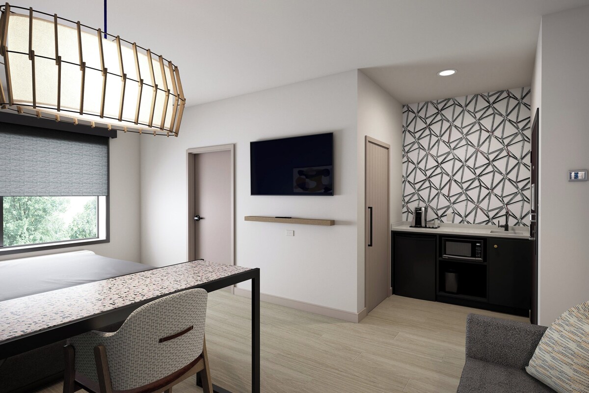 Un espace de vie moderne et compact comprenant un coin repas, une kitchenette et une grande fenêtre.