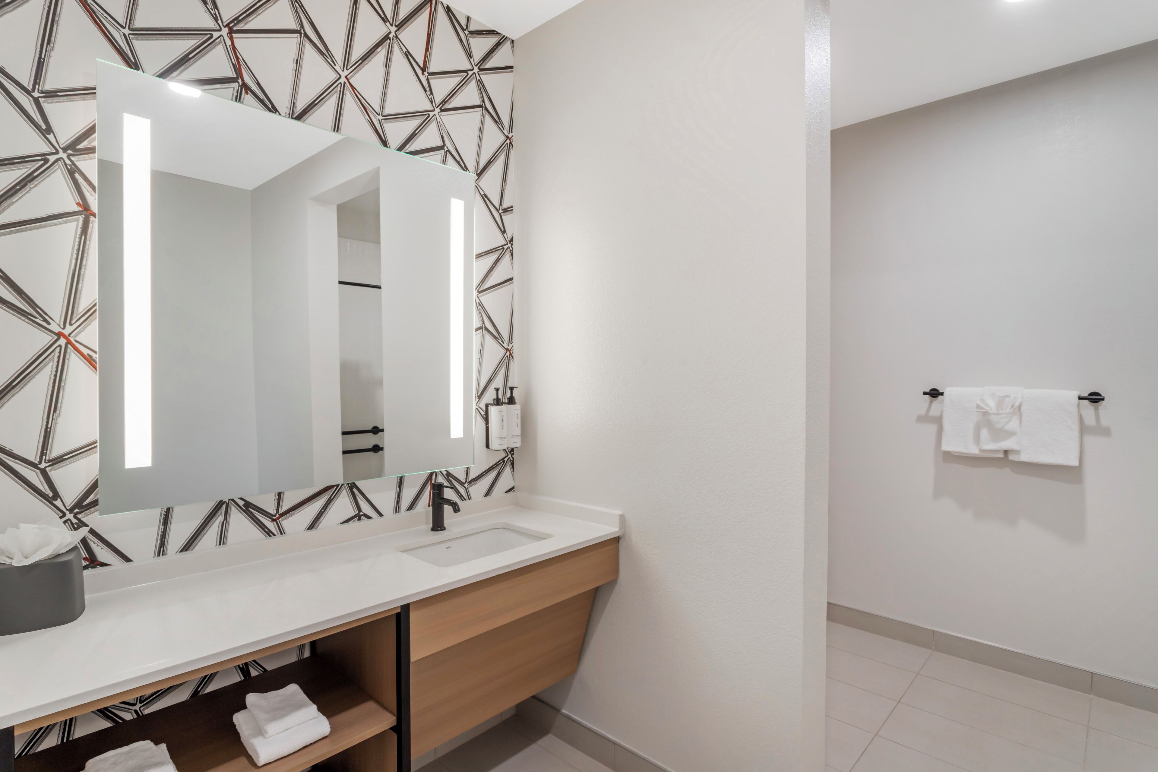 A modern bathroom with a white vanity, a large mirror, and a towel rack.