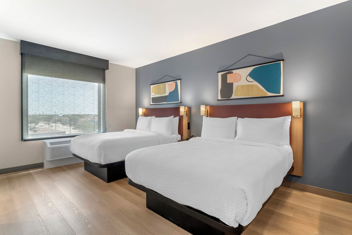 Een hotelkamer met twee bedden, een groot raam en abstracte wanddecoratie.