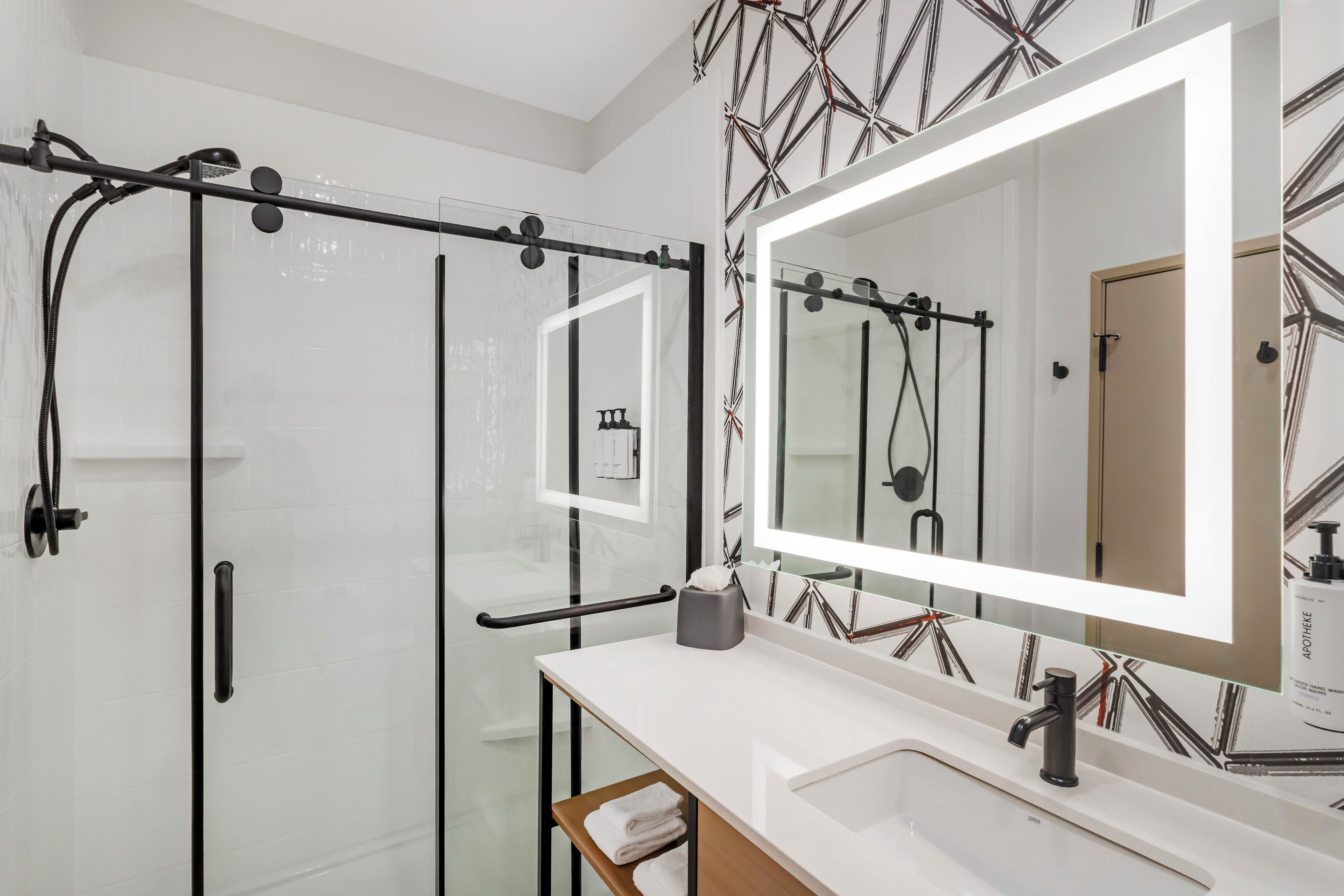 A modern bathroom with a glass shower enclosure, a large mirror, and a white sink.