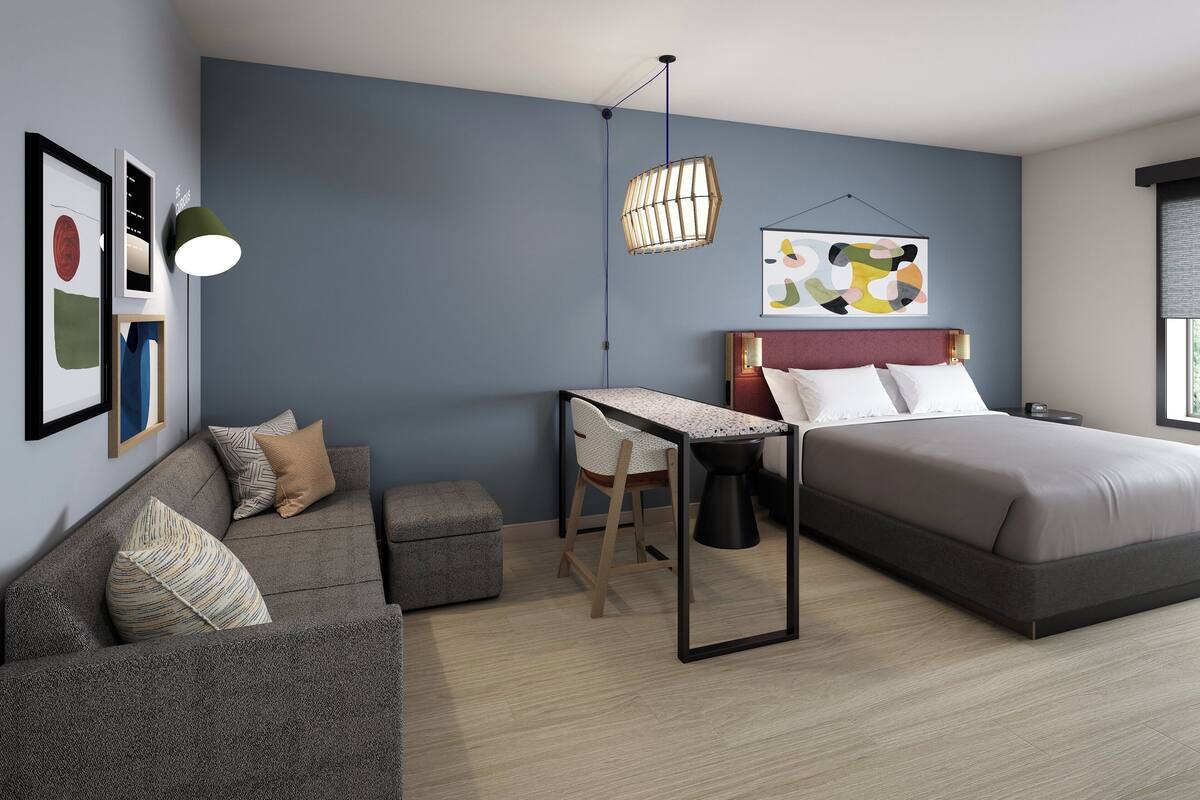 Une chambre moderne avec un lit, un bureau, une chaise et un luminaire suspendu.