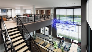 Un amplio vestíbulo de hotel de varios niveles con un diseño moderno, que incluye una escalera, zonas de estar y grandes ventanales con vistas a la calle.