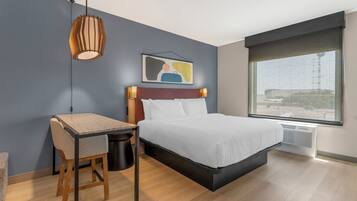 A modern hotel room with a bed, desk, chair, and a large window.