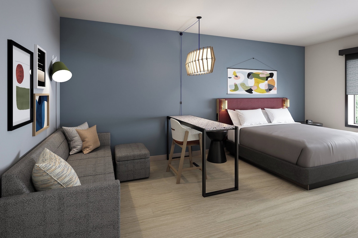 Une chambre moderne avec un lit, un bureau, une chaise et un luminaire suspendu.