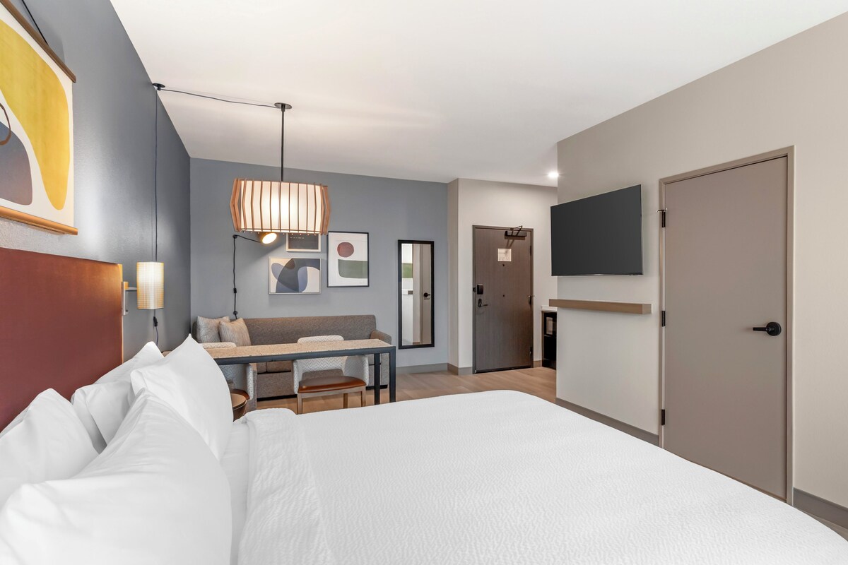 Une chambre d’hôtel avec un grand lit, un bureau avec une chaise, un téléviseur fixé au mur et une porte.