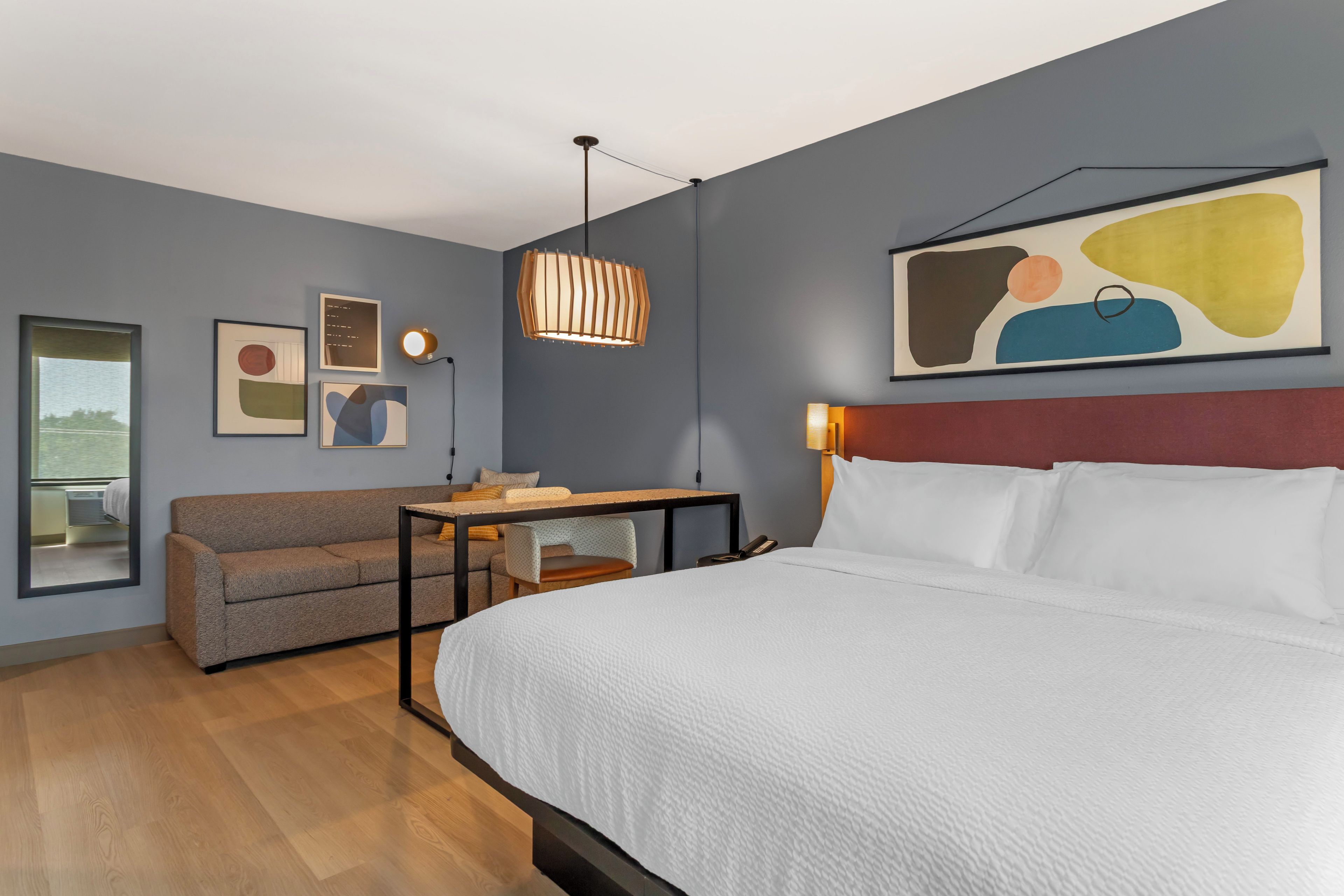 Ein modernes Hotelzimmer mit einem großen Bett, einem Sofa, einem Schreibtisch und einem Gemälde an der Wand.