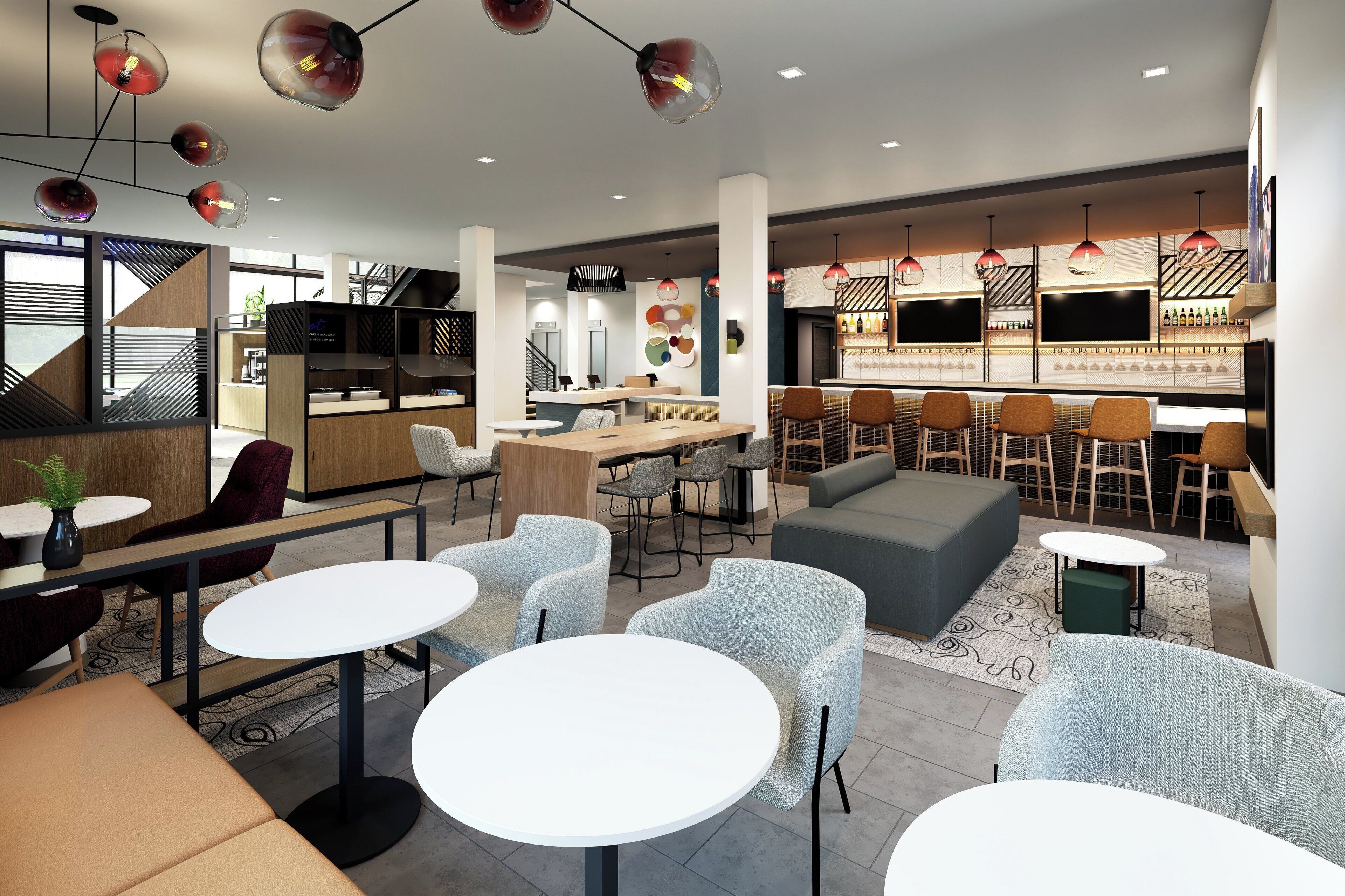 A modern interior with round tables, grey chairs, a bar area, and a staircase.