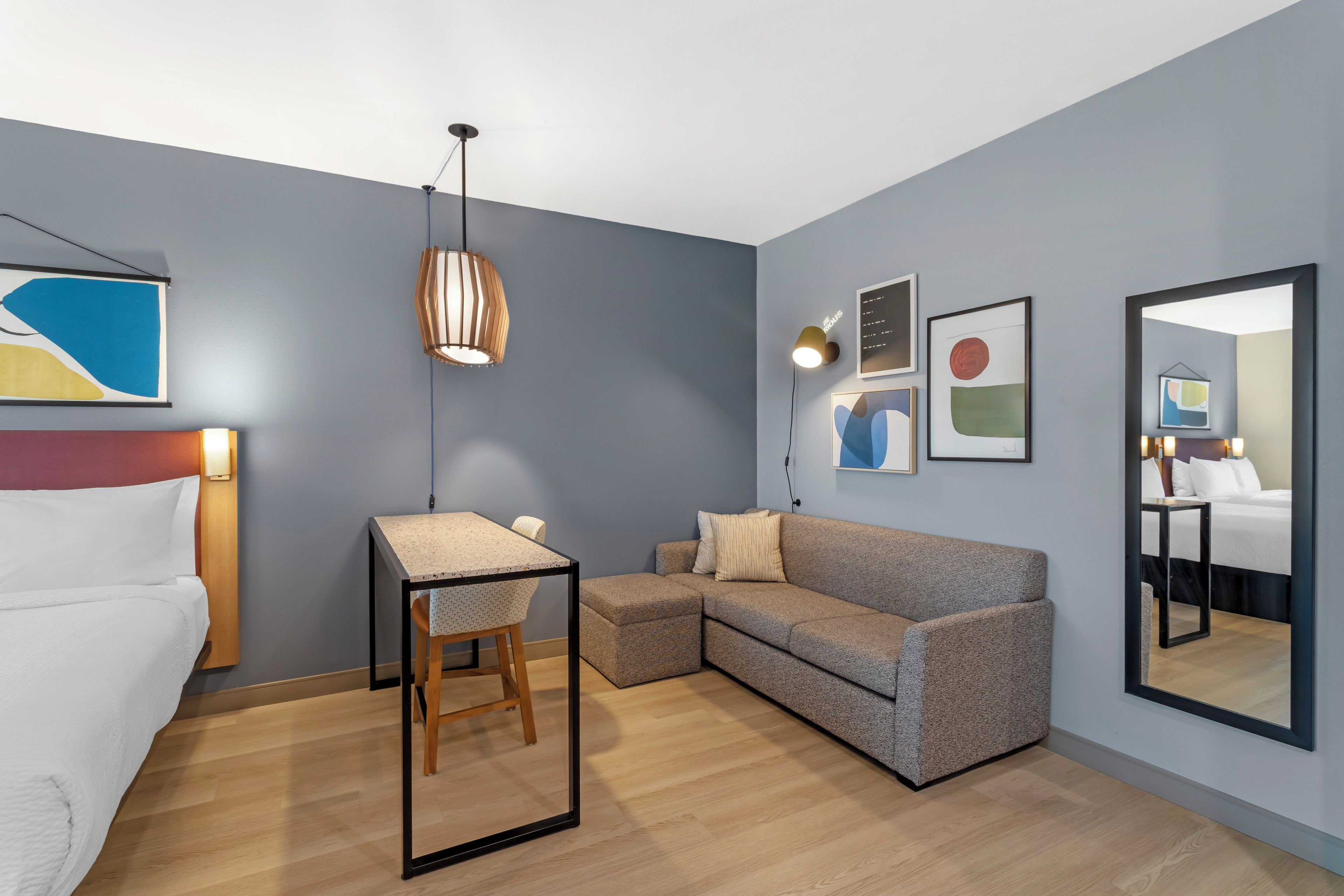 A modern hotel room with a bed, a desk, a sofa, and a large mirror.