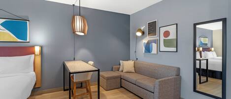 A modern hotel room with a bed, a desk, a sofa, and a large mirror.