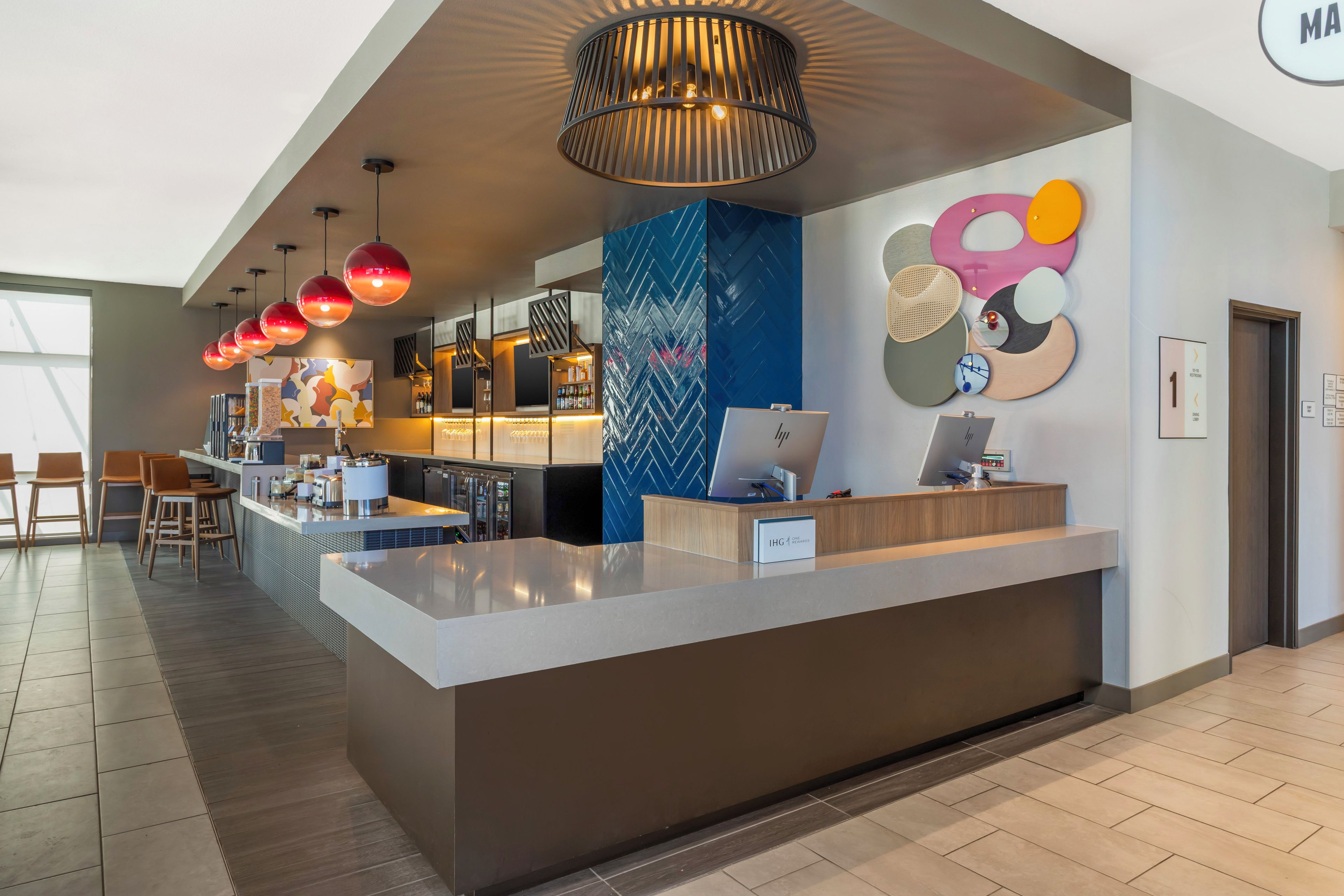 A modern hotel lobby with a reception desk, seating area, and a large window providing natural light.