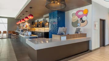 A modern hotel lobby with a reception desk, seating area, and a large window providing natural light.