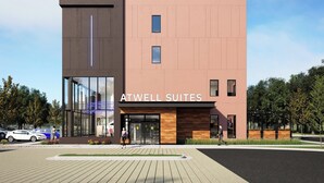 Un hotel moderno con entrada de vidrio, señalización ATWELL SUITES y un área de estacionamiento.