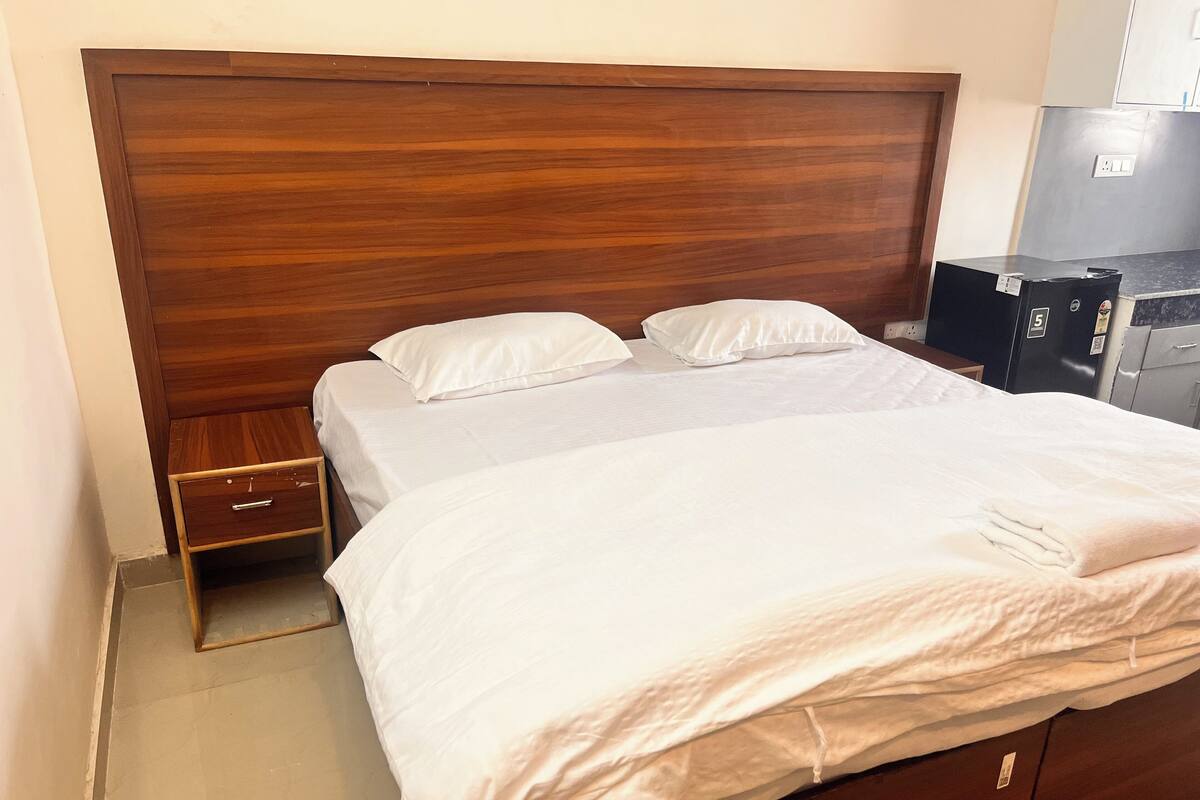 Hotellihuone, jossa on puinen sängynpääty, kaksi erillistä sänkyä, yöpöytä ja pieni laatikosto.