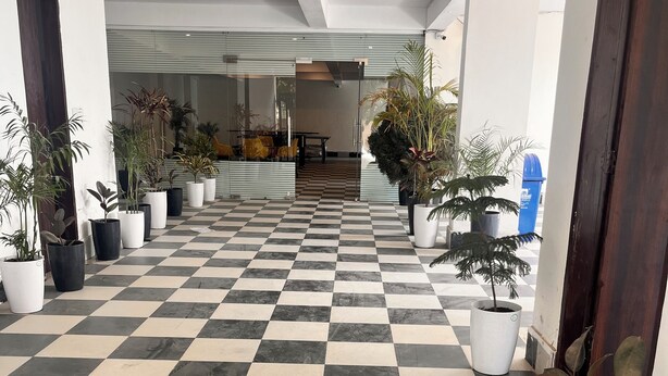 Un vestíbulo de hotel con piso de cuadros, plantas en macetas y una escalera que sube a otro nivel.