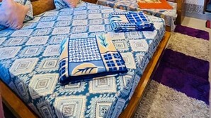 Ein Schlafzimmer mit einem großen Bett, zwei Einzelbetten, Holzvertäfelung, einem Deckenventilator und einem gerahmten Bild an der Wand.