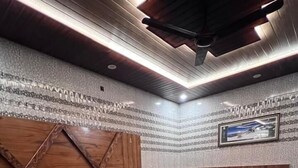 Ein Schlafzimmer mit einem großen Bett, zwei Nachttischen, einem hölzernen Kopfteil, einem an der Wand befestigten Fernseher und einer Wand mit Muster.