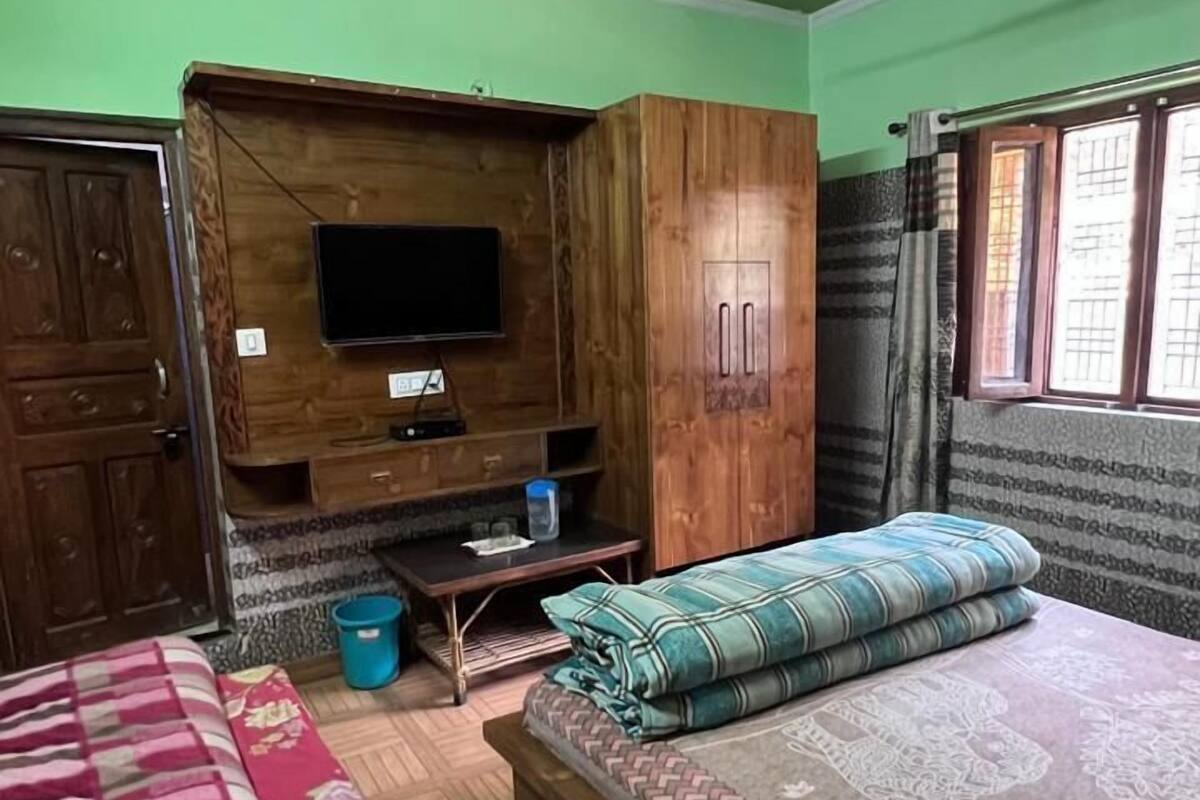 A bedroom with a bed, two bedside tables, a wooden wardrobe, a ceiling fan, and a television.
