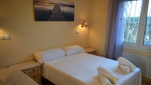 A neatly made bed with white linens and towels, a bedside table, a wall-mounted lamp, and a painting of a pier on the wall.