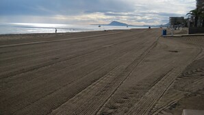 A wide sandy beach with a clear view of the ocean and distant mountains.