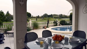 Un coin repas avec une table mise pour le petit-déjeuner, donnant sur une piscine et un jardin.