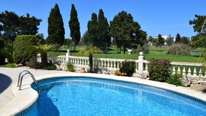 Une piscine bordée de pierres, entourée d’une clôture blanche et agrémentée de diverses plantes.