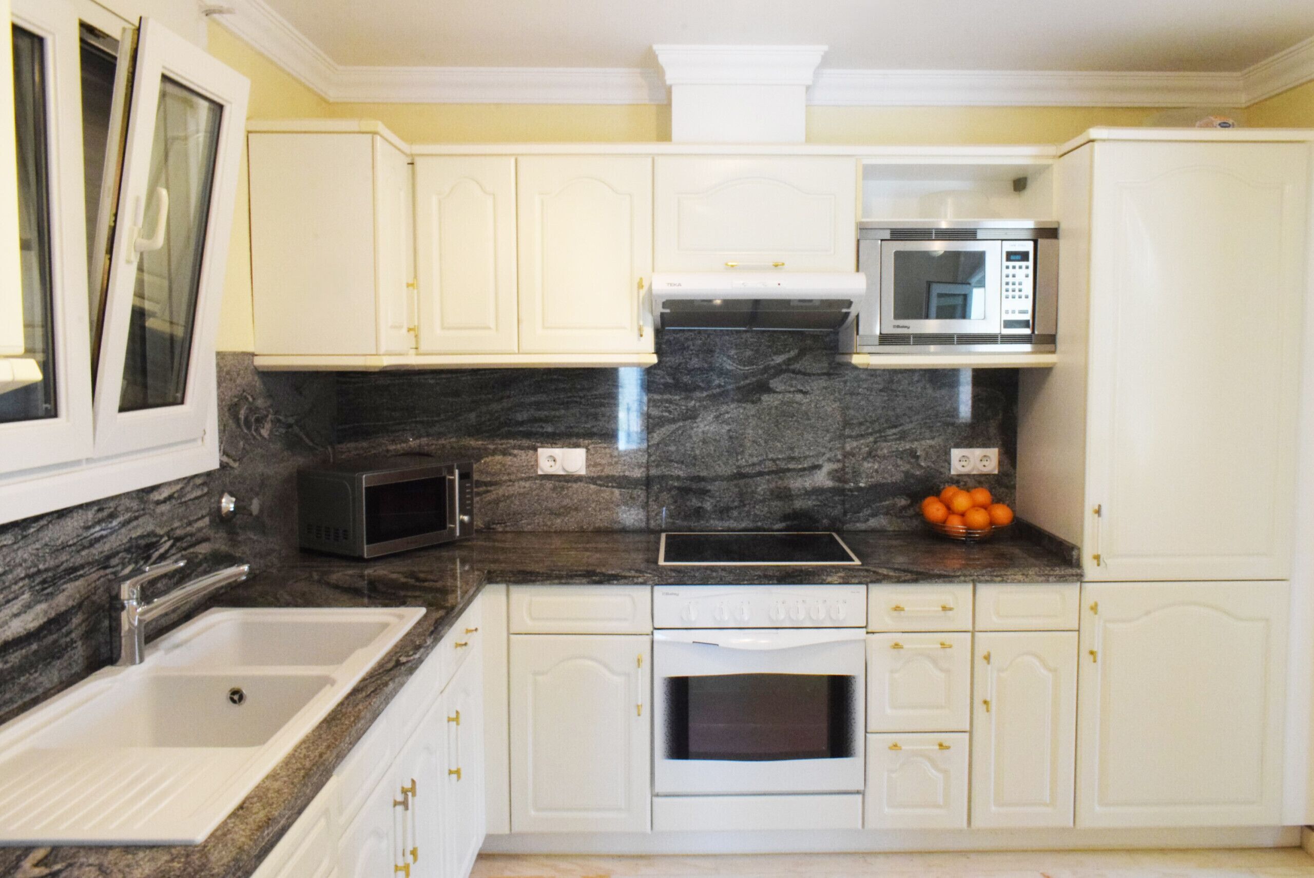 A kitchen with white cabinets, a granite countertop, a microwave, a sink, and an oven.