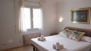 Une chambre à coucher avec un lit, des oreillers, une fenêtre avec des rideaux, un radiateur et une lampe fixée au mur.