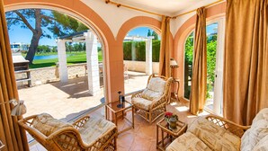 Un patio soleado con muebles de mimbre, vistas a un campo de golf y una pérgola.