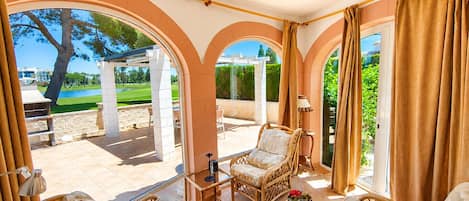 A sunlit patio with wicker furniture, a view of a golf course, and a pergola structure.