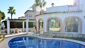Una piscina con zona de patio, un área de estar cubierta y un edificio con ventanales arqueados.