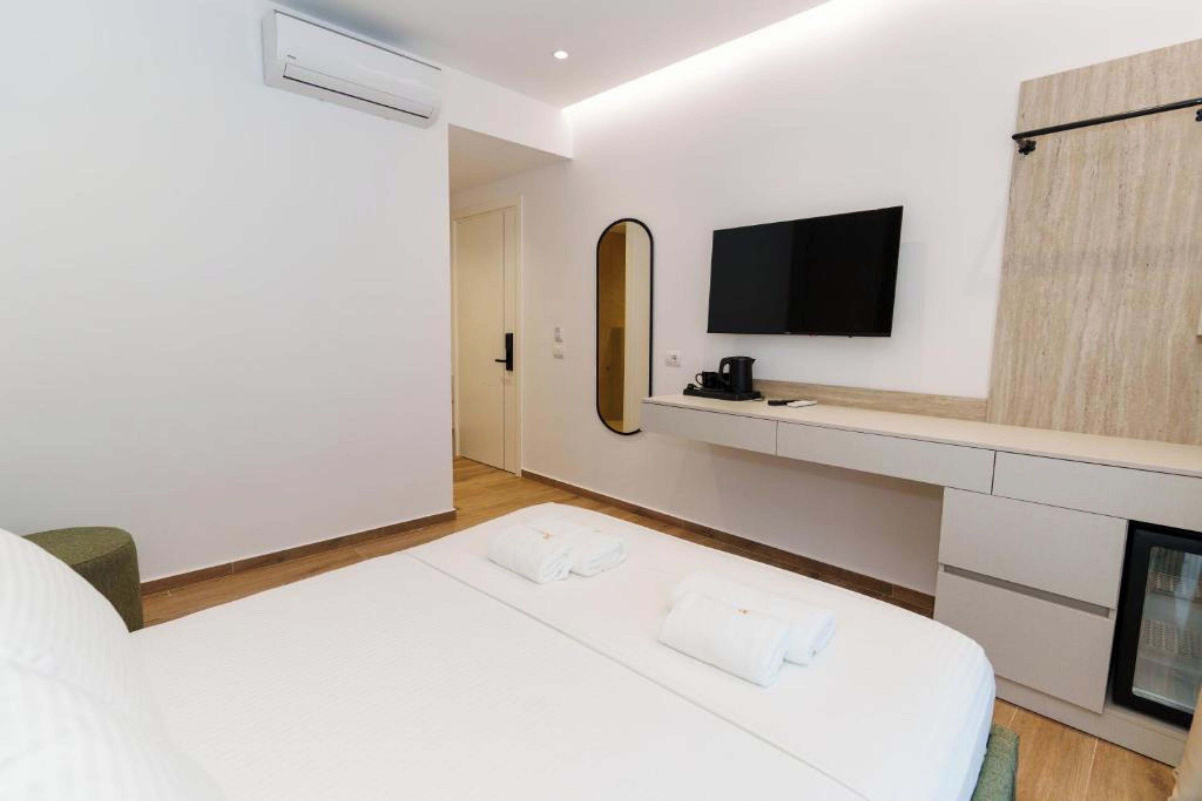 A modern hotel room with a bed, a flat-screen TV, a mirror, a small desk with a coffee maker, and a fireplace.