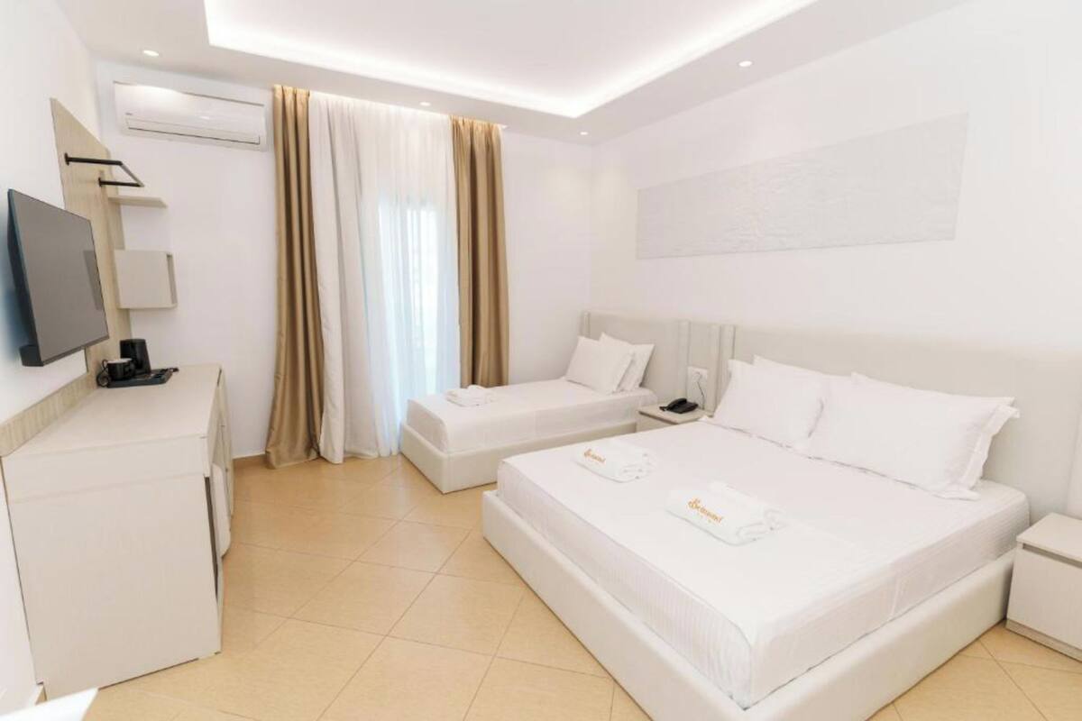 Una habitación de hotel con una cama grande, una cama más pequeña, un escritorio con televisor y una ventana con cortinas.